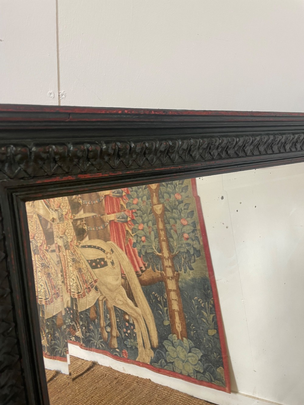 A large rectangular wall mirror with a dark, distressed carved wooden frame resting against a white wall. View IV