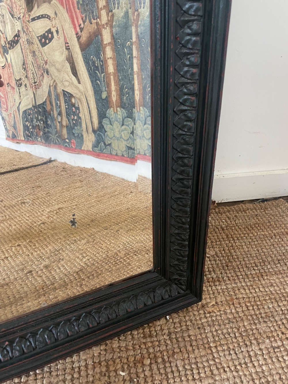 A large rectangular wall mirror with a dark, distressed carved wooden frame resting against a white wall. View V