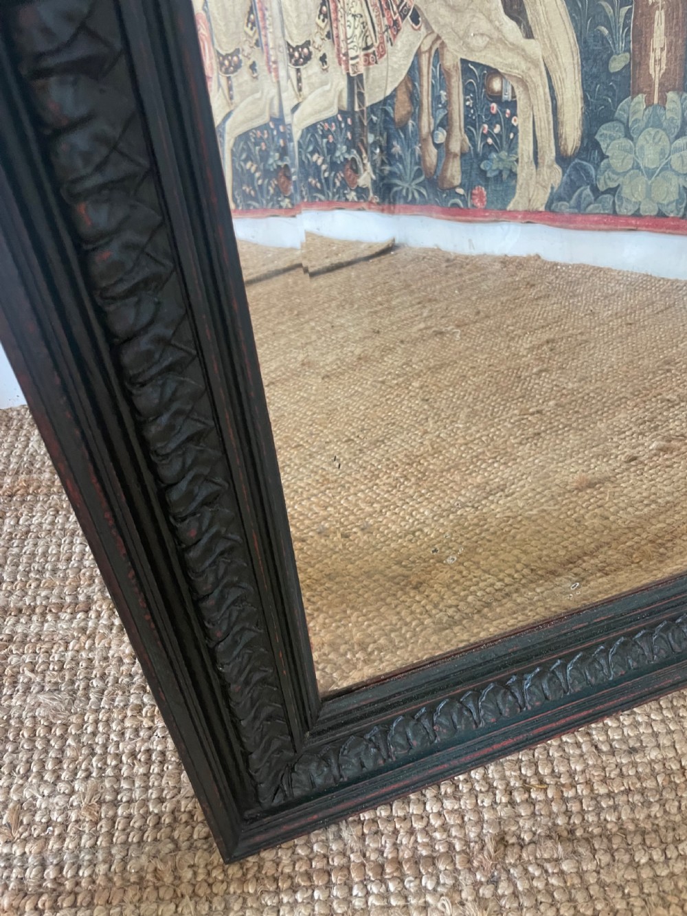 A large rectangular wall mirror with a dark, distressed carved wooden frame resting against a white wall. View VII