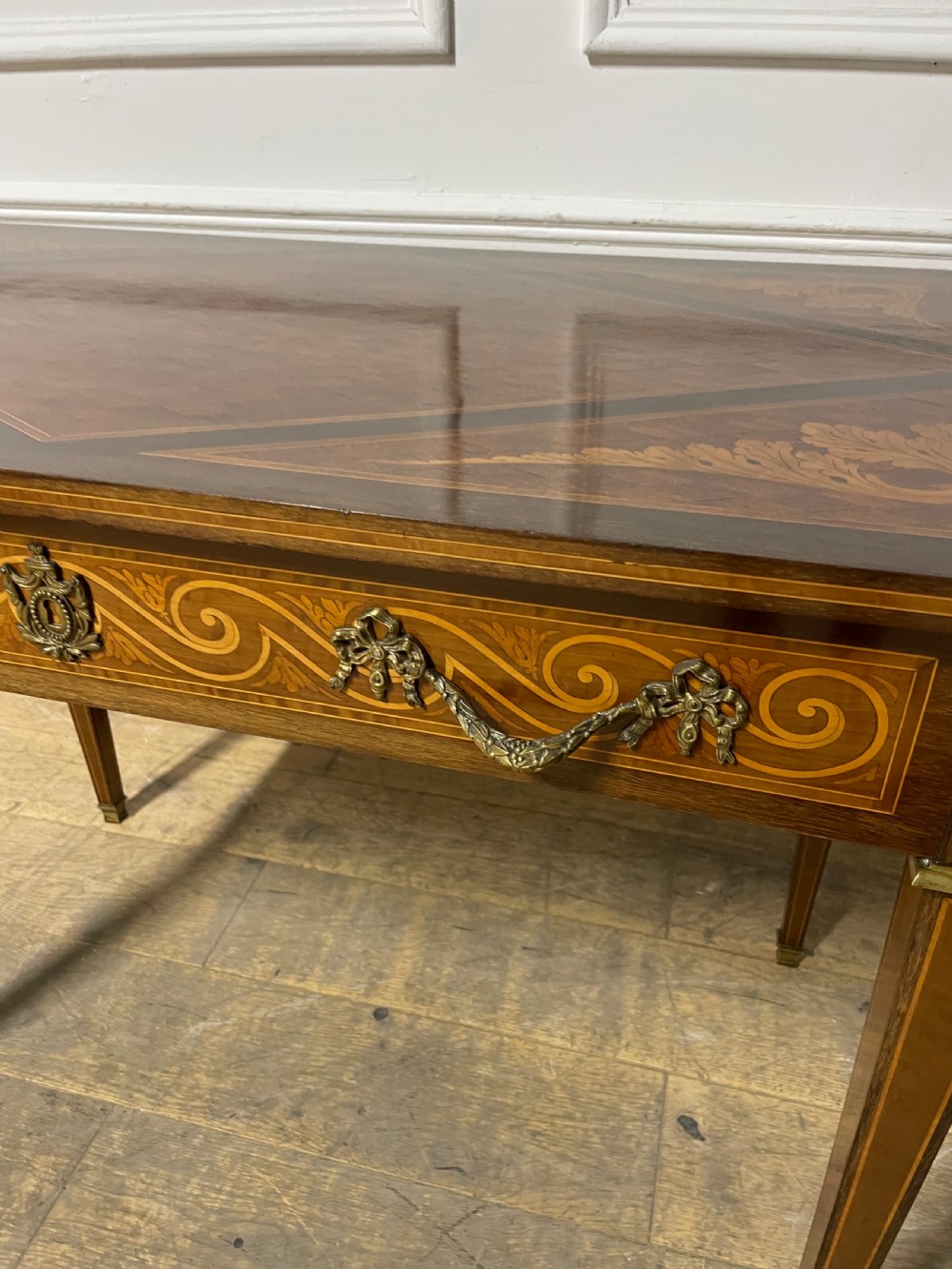 A rectangular antique wooden writing table featuring intricate geometric and floral marquetry on the top and frieze drawer, accented with cast brass mounts and tapering legs. View V