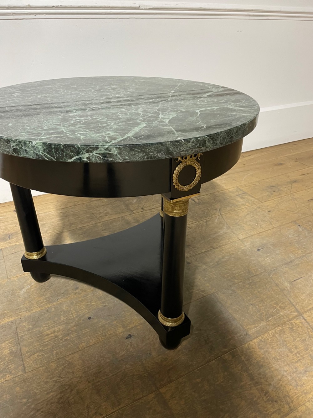 A circular Empire style table featuring a polished green marble top, ebonised column legs with gilt brass mounts, and a concave triform base. View V