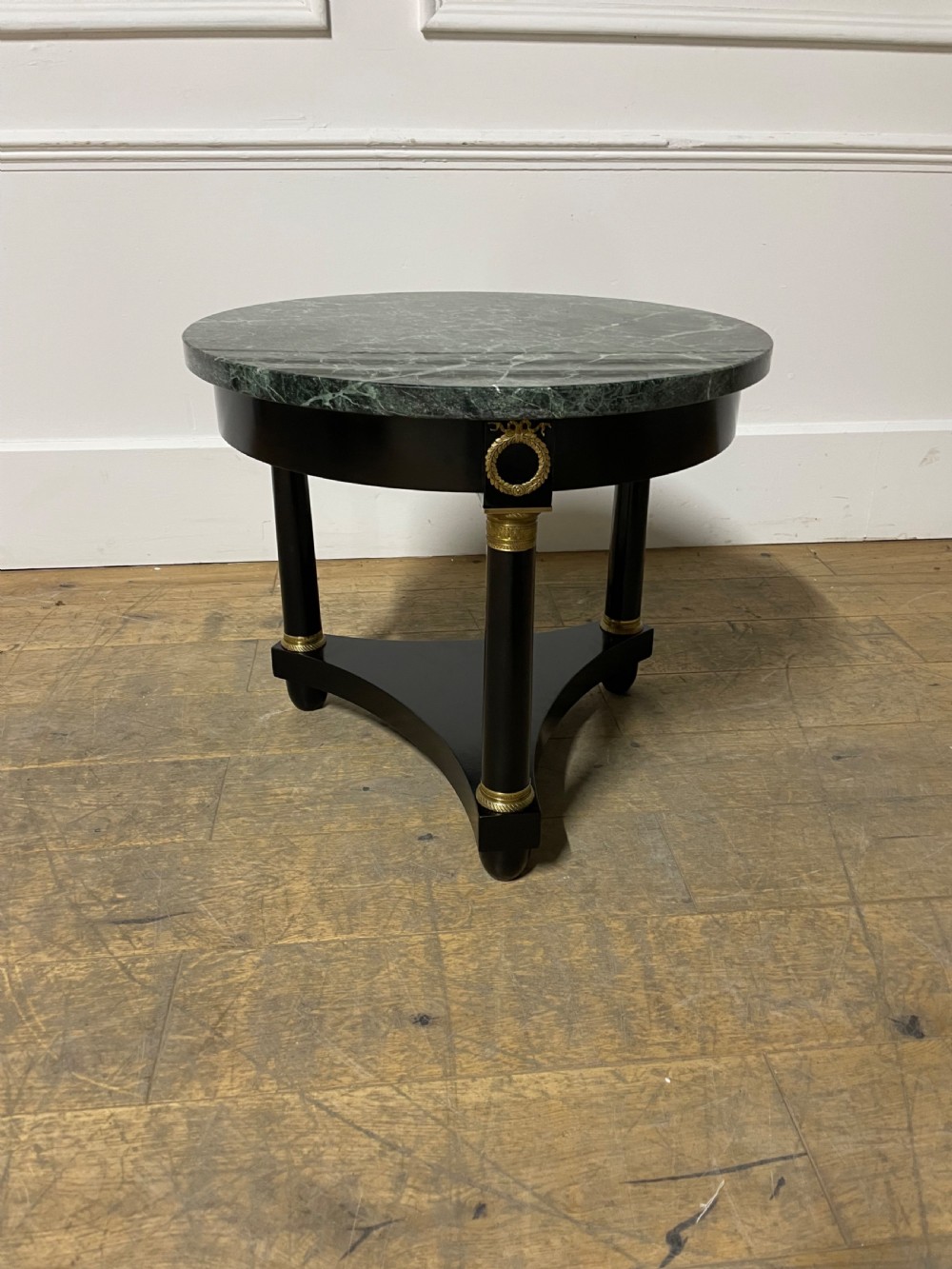 A circular Empire style table featuring a polished green marble top, ebonised column legs with gilt brass mounts, and a concave triform base. View VI