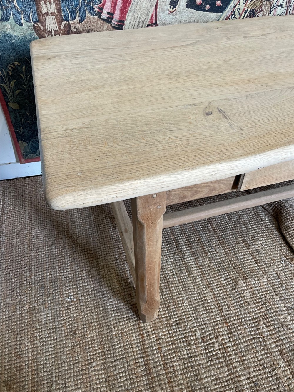 A long light oak farmhouse table featuring a rectangular plank top, two frieze drawers with dark metal handles, and square legs joined by a low stretcher. View VI