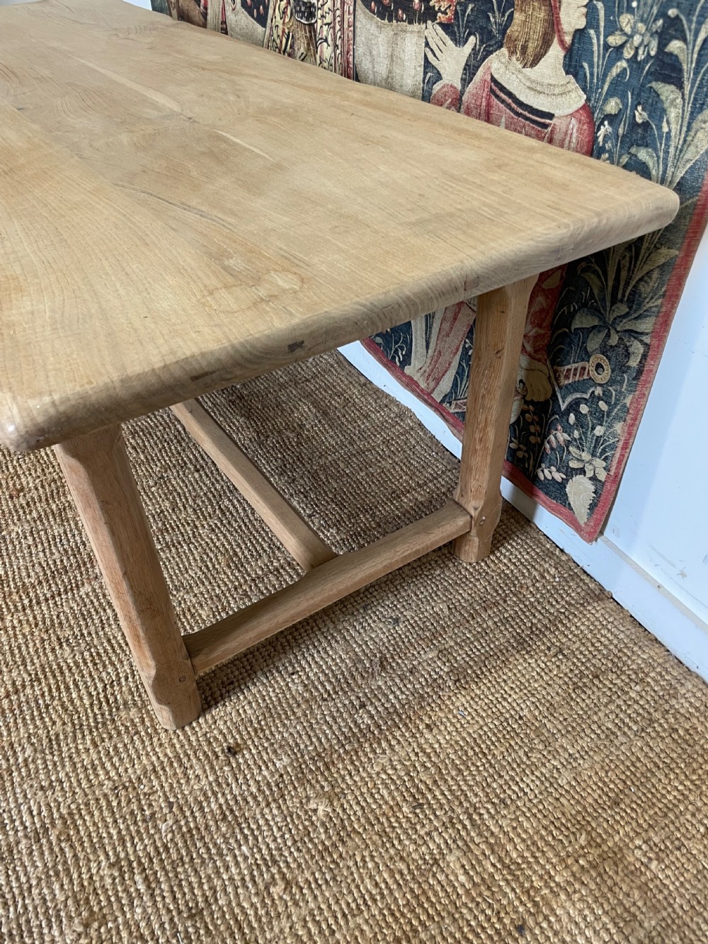 A long light oak farmhouse table featuring a rectangular plank top, two frieze drawers with dark metal handles, and square legs joined by a low stretcher. View X
