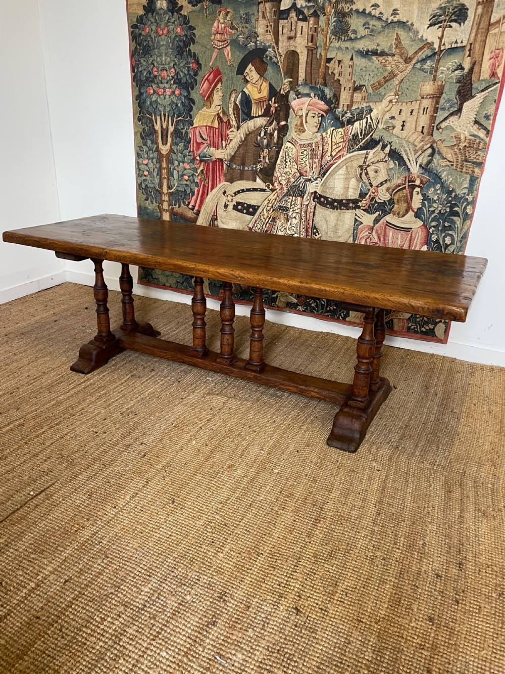 A long rectangular wooden refectory table featuring a plank top and turned leg supports joined by a low stretcher.