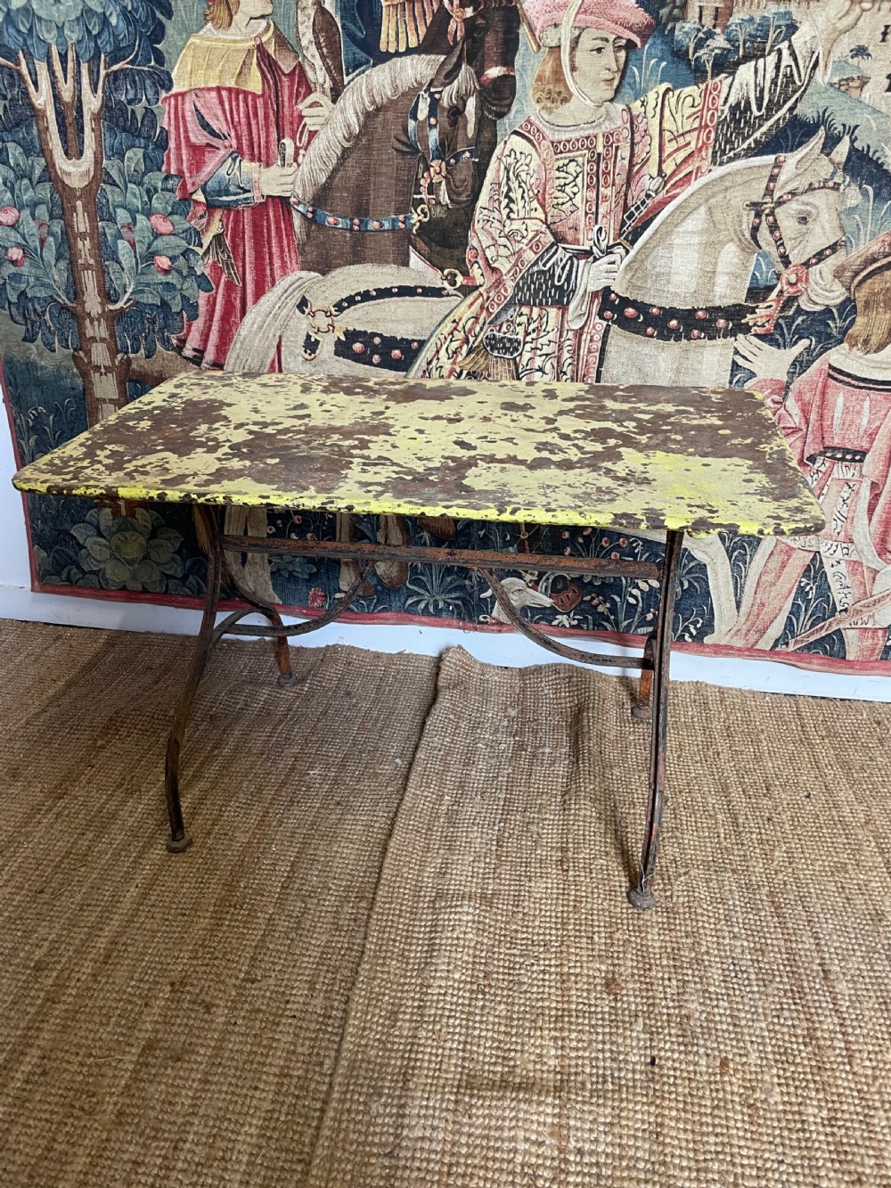 An antique rectangular metal garden table with a distressed yellow painted top and curved iron legs.