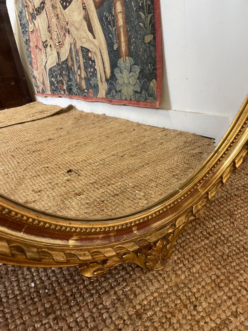 An oval wall mirror featuring a carved gold gilt frame topped with an elaborate ribbon bow scroll. View III