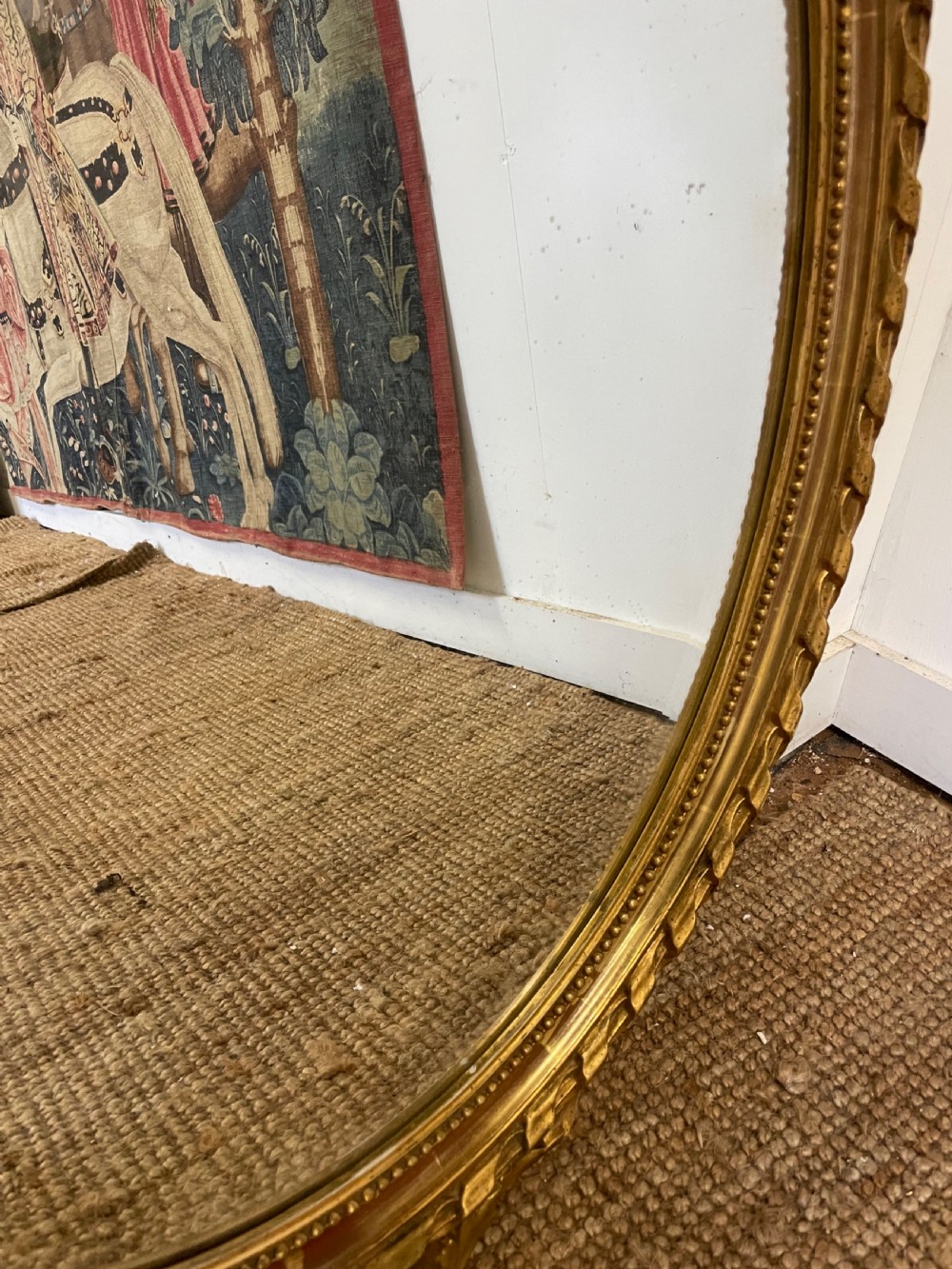 An oval wall mirror featuring a carved gold gilt frame topped with an elaborate ribbon bow scroll. View IV