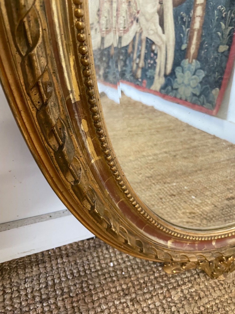 An oval wall mirror featuring a carved gold gilt frame topped with an elaborate ribbon bow scroll. View VI