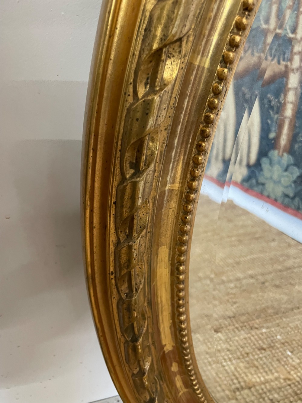 An oval wall mirror featuring a carved gold gilt frame topped with an elaborate ribbon bow scroll. View VII