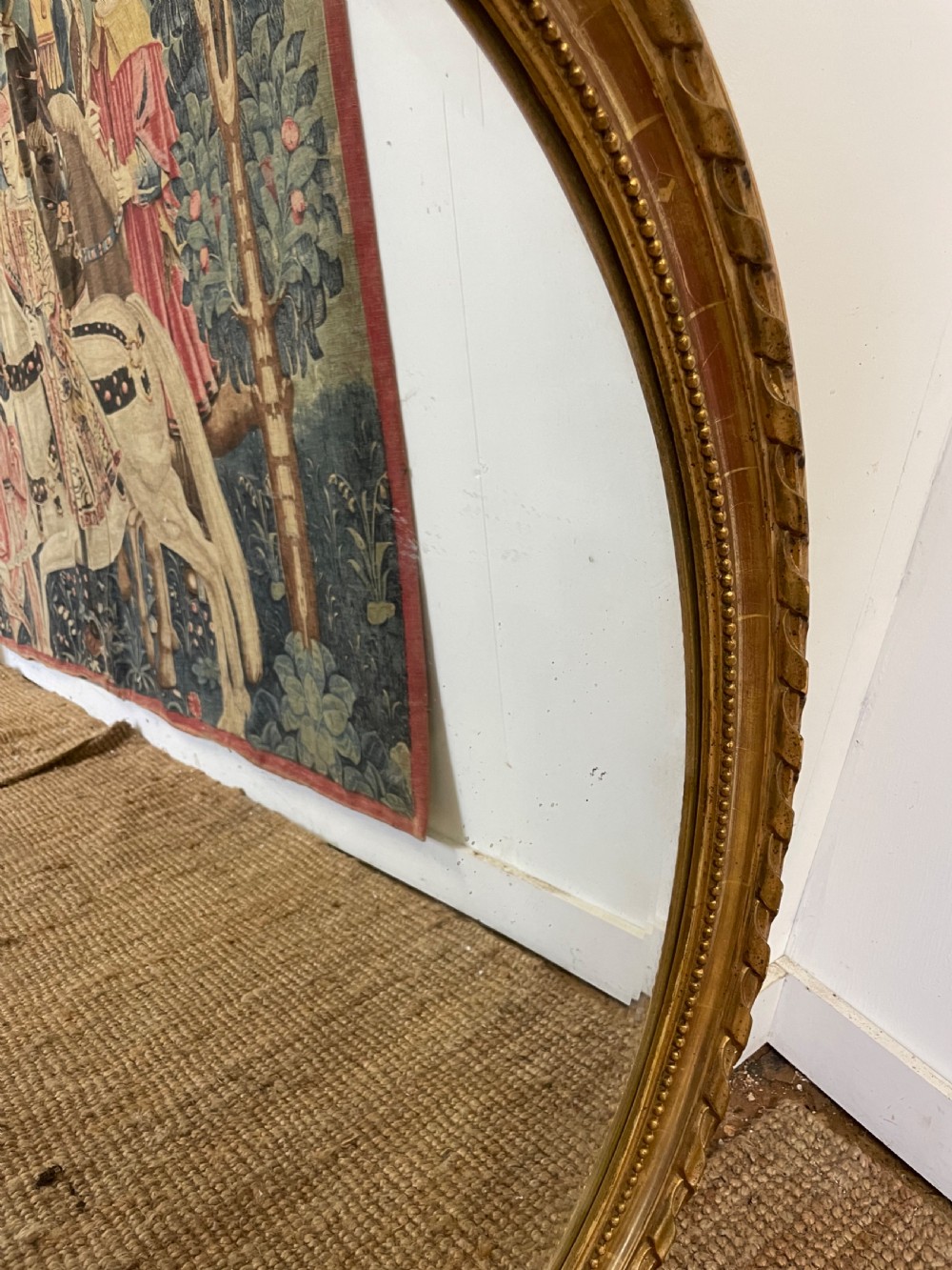 An oval wall mirror featuring a carved gold gilt frame topped with an elaborate ribbon bow scroll. View IX