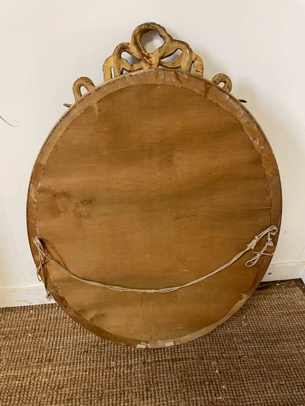An oval wall mirror featuring a carved gold gilt frame topped with an elaborate ribbon bow scroll. View X