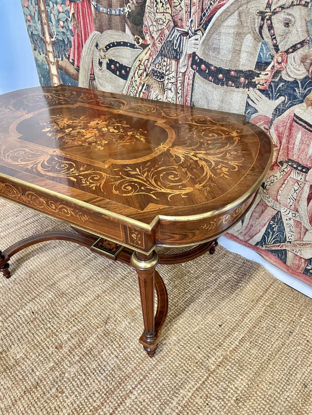 An antique rosewood writing table featuring intricate floral marquetry inlay across the top and stretcher base, complemented by brass edging and turned supports. View II