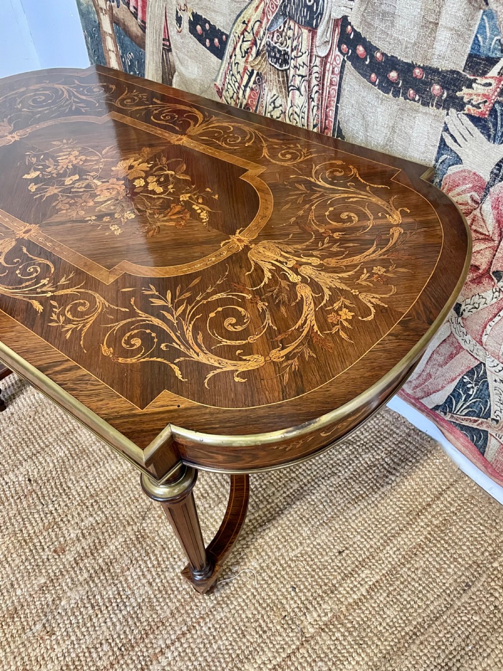 An antique rosewood writing table featuring intricate floral marquetry inlay across the top and stretcher base, complemented by brass edging and turned supports. View III