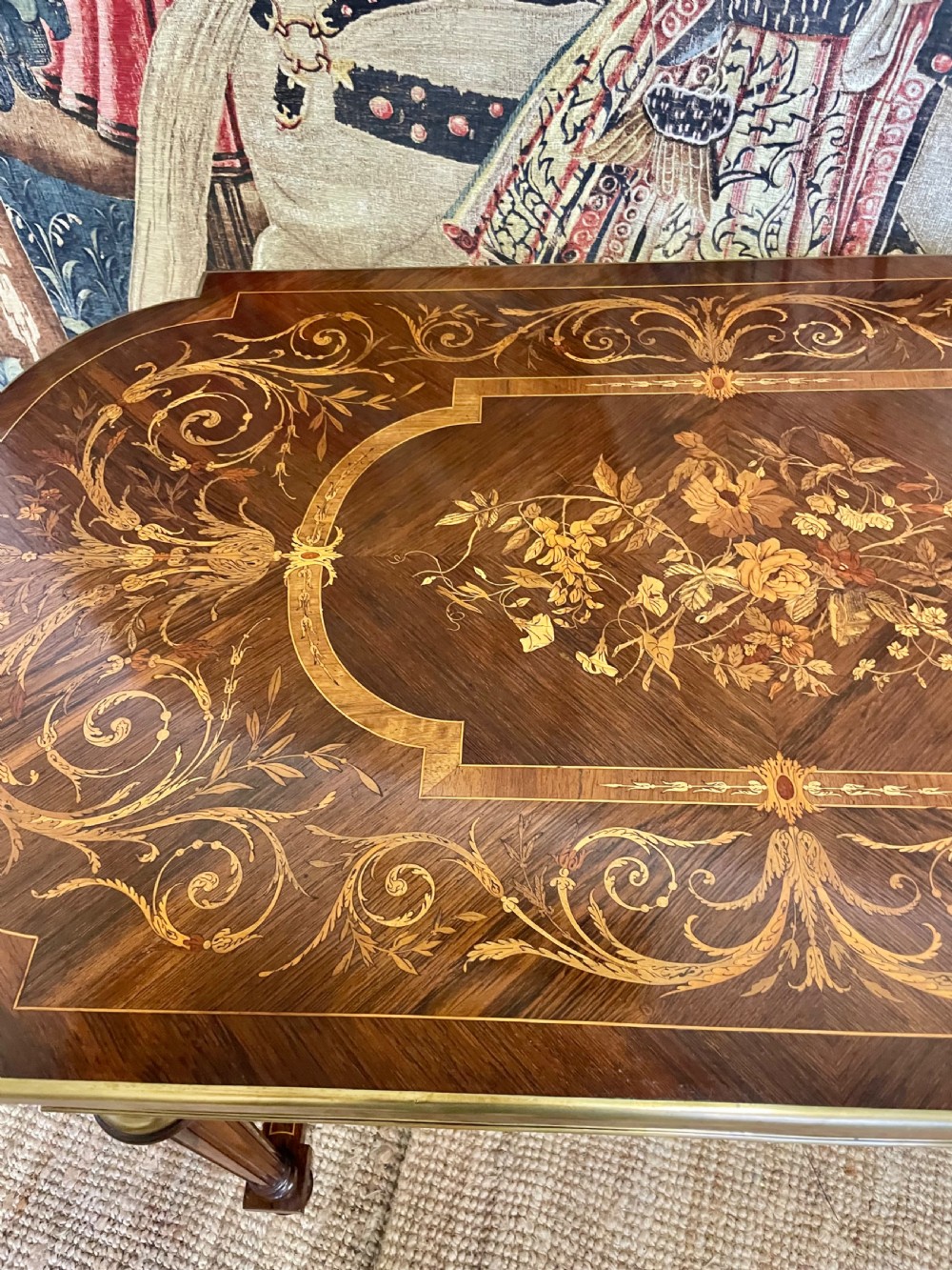 An antique rosewood writing table featuring intricate floral marquetry inlay across the top and stretcher base, complemented by brass edging and turned supports. View V