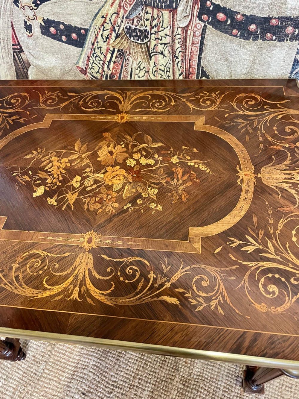 An antique rosewood writing table featuring intricate floral marquetry inlay across the top and stretcher base, complemented by brass edging and turned supports. View VI