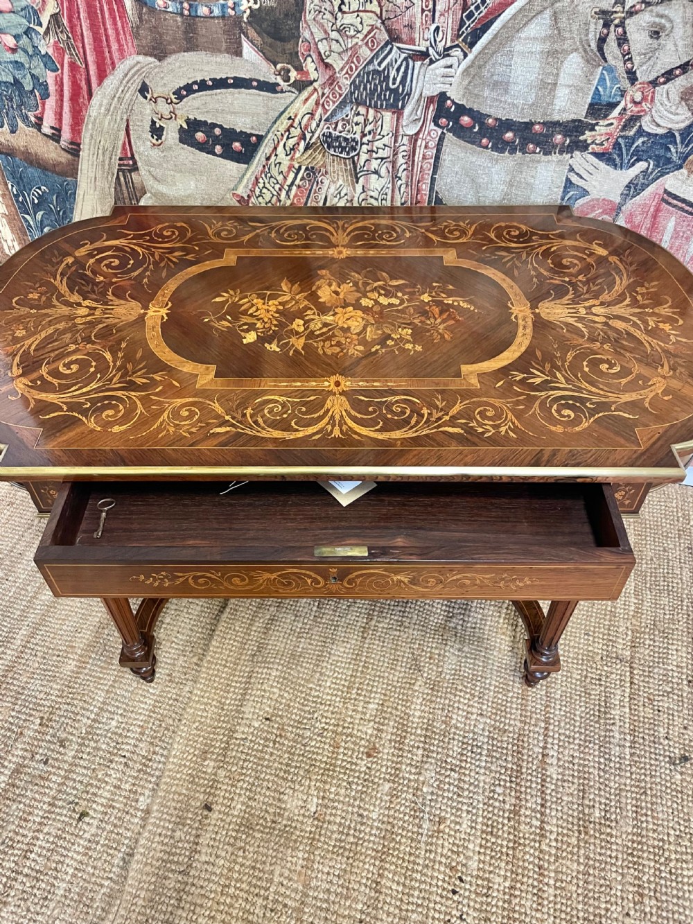 An antique rosewood writing table featuring intricate floral marquetry inlay across the top and stretcher base, complemented by brass edging and turned supports. View X