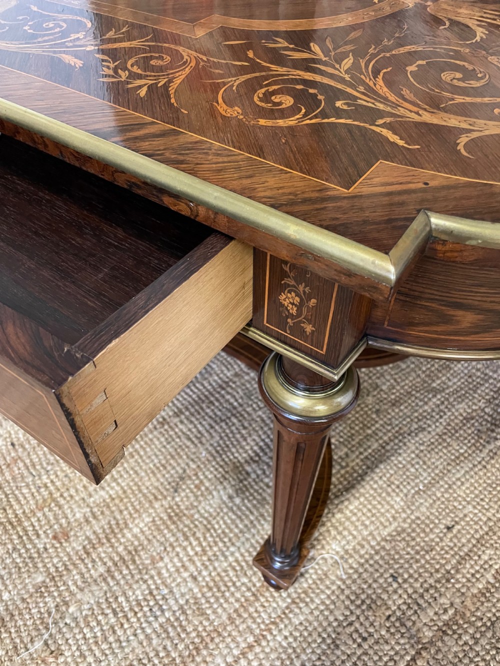 An antique rosewood writing table featuring intricate floral marquetry inlay across the top and stretcher base, complemented by brass edging and turned supports. View XI
