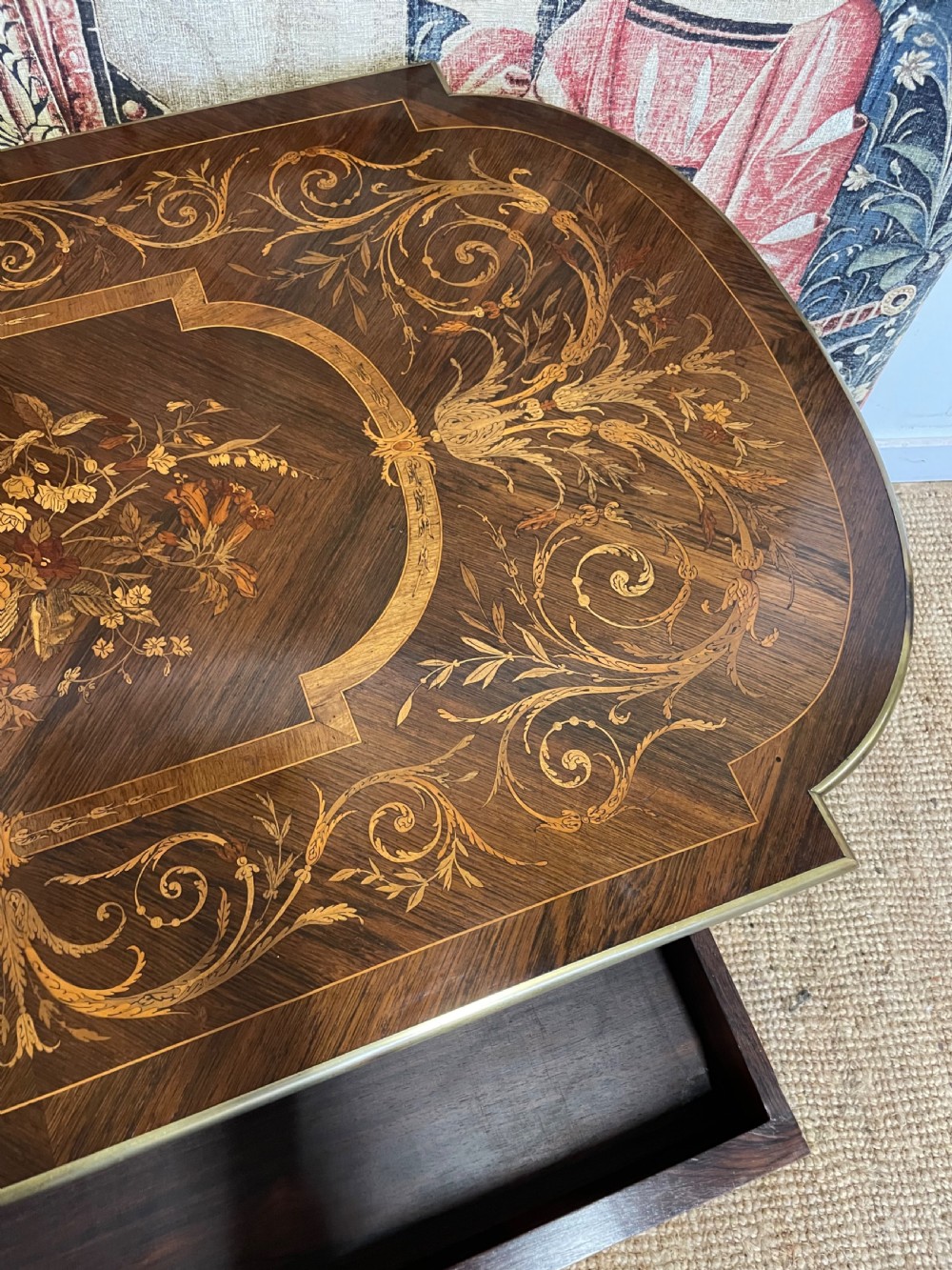 An antique rosewood writing table featuring intricate floral marquetry inlay across the top and stretcher base, complemented by brass edging and turned supports. View XIII
