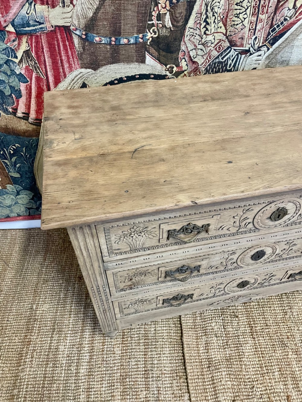 An early 19th-century scrubbed oak commode featuring three hand-carved drawers decorated with floral basket motifs and brass swing handles. View VII