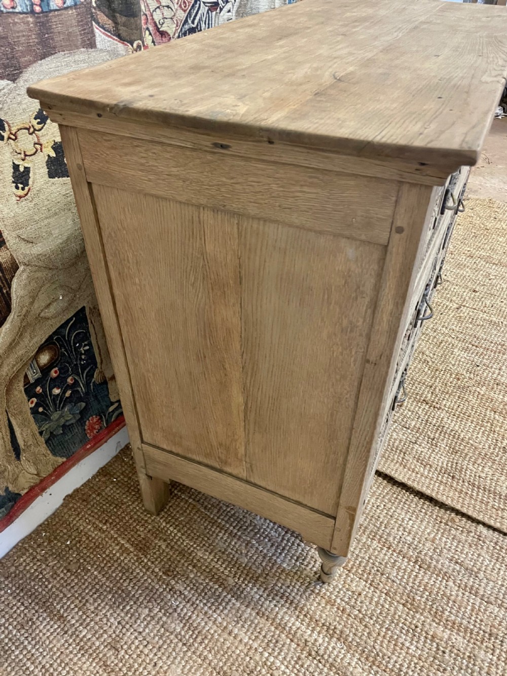 An early 19th-century scrubbed oak commode featuring three hand-carved drawers decorated with floral basket motifs and brass swing handles. View IX