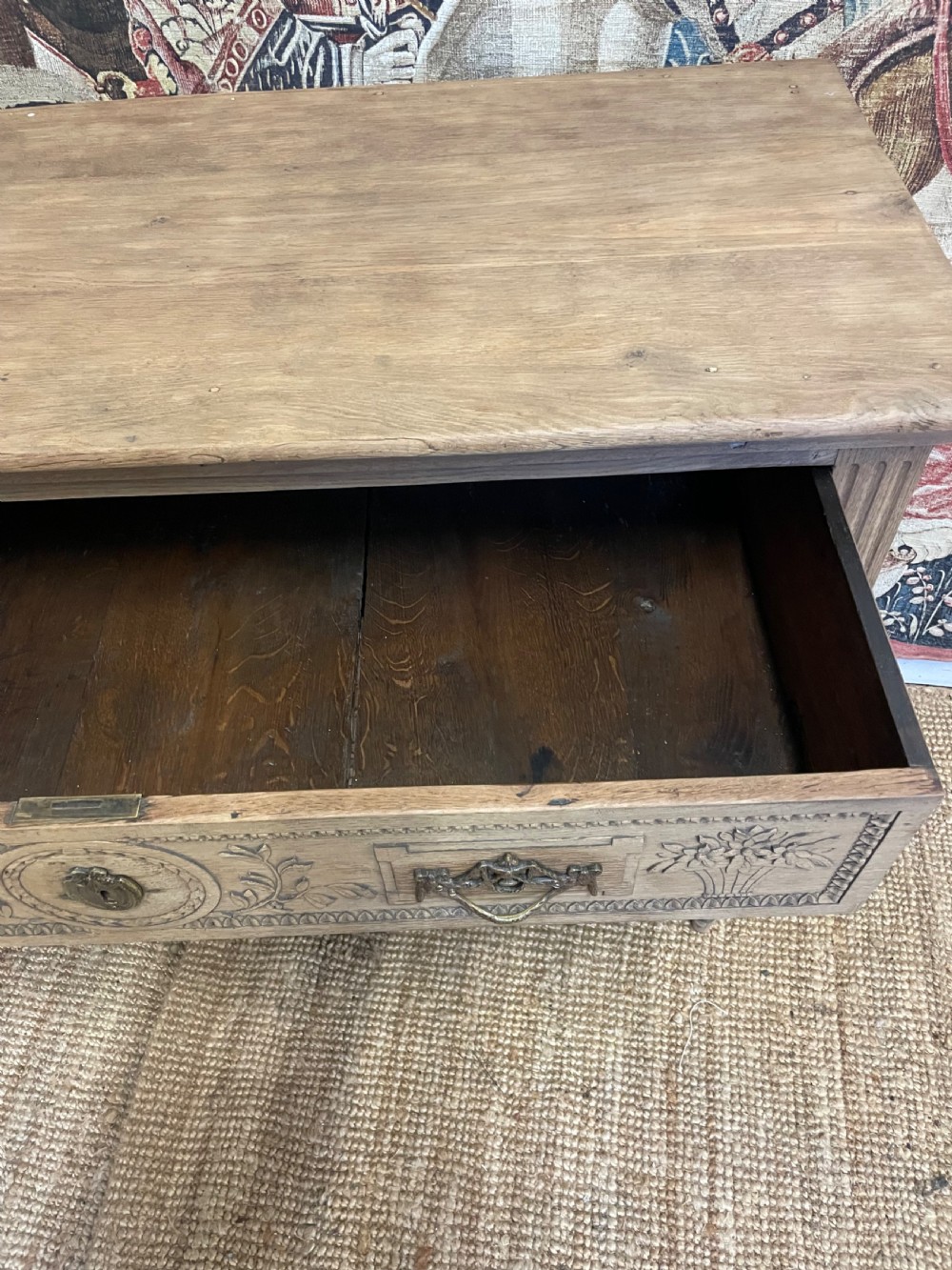 An early 19th-century scrubbed oak commode featuring three hand-carved drawers decorated with floral basket motifs and brass swing handles. View XIV