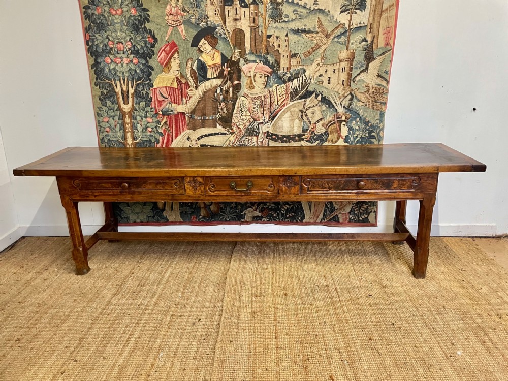 An elongated antique walnut console table featuring three drawers with brass hardware and low stretcher supports.