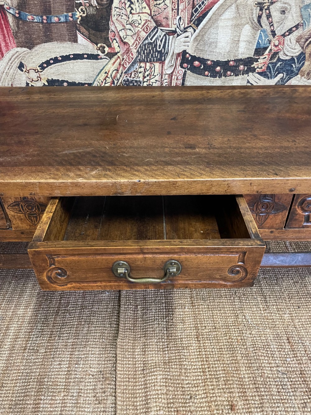 An elongated antique walnut console table featuring three drawers with brass hardware and low stretcher supports. View XII