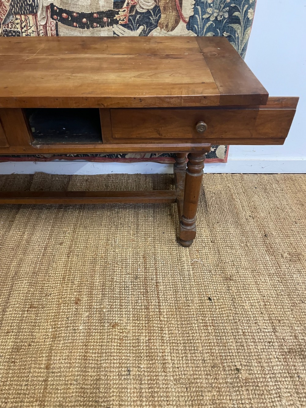 A long rectangular antique cherrywood console table featuring three frieze drawers with small brass knobs and turned legs connected by a low stretcher. View VI