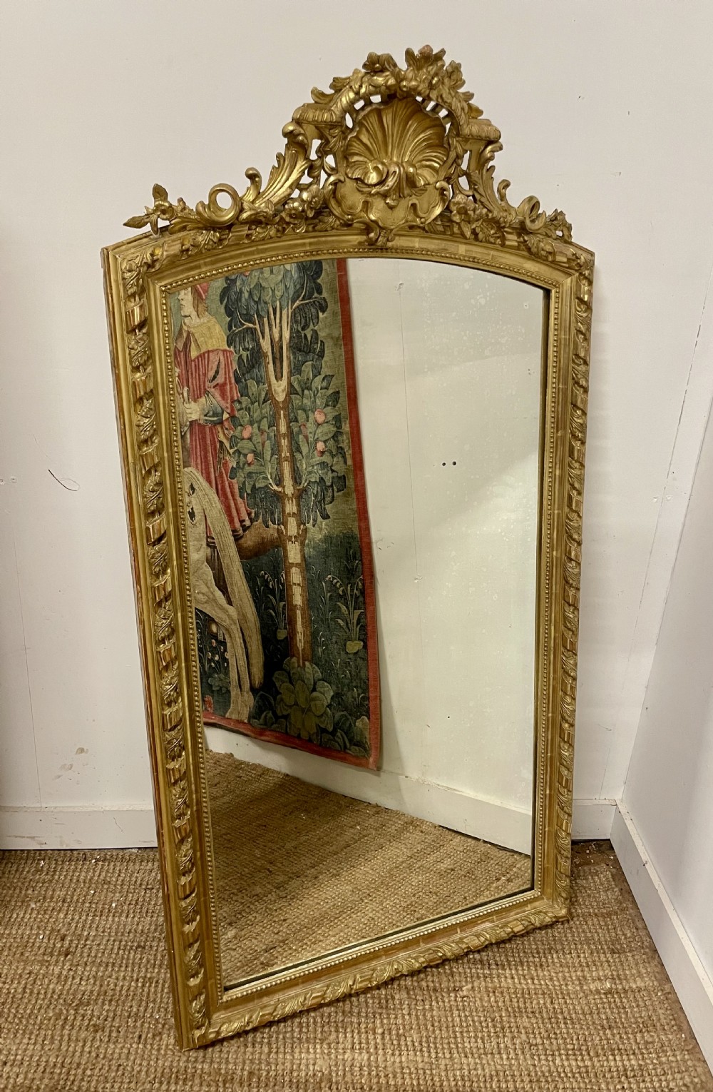 A late nineteenth-century gilded wall mirror featuring an arched top, carved shell cresting, and foliate moulding on the frame.