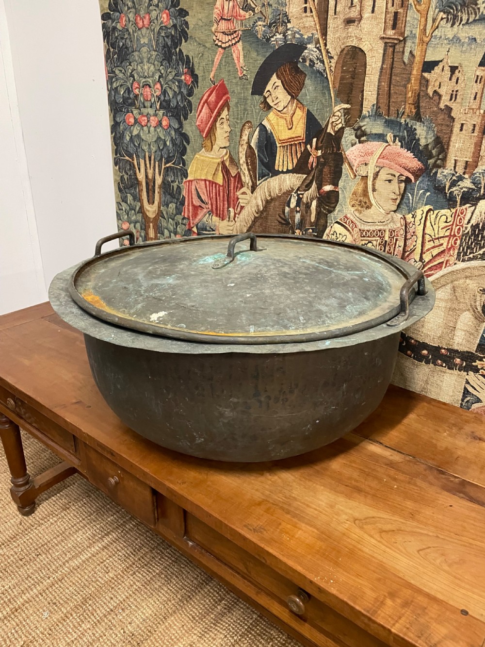 A large round antique copper vessel featuring a fitted lid, twin iron loop handles, and a deep patinated surface with verdigris tones. View II