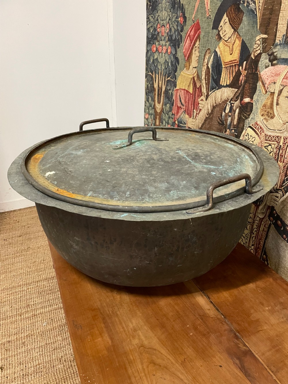 A large round antique copper vessel featuring a fitted lid, twin iron loop handles, and a deep patinated surface with verdigris tones. View III