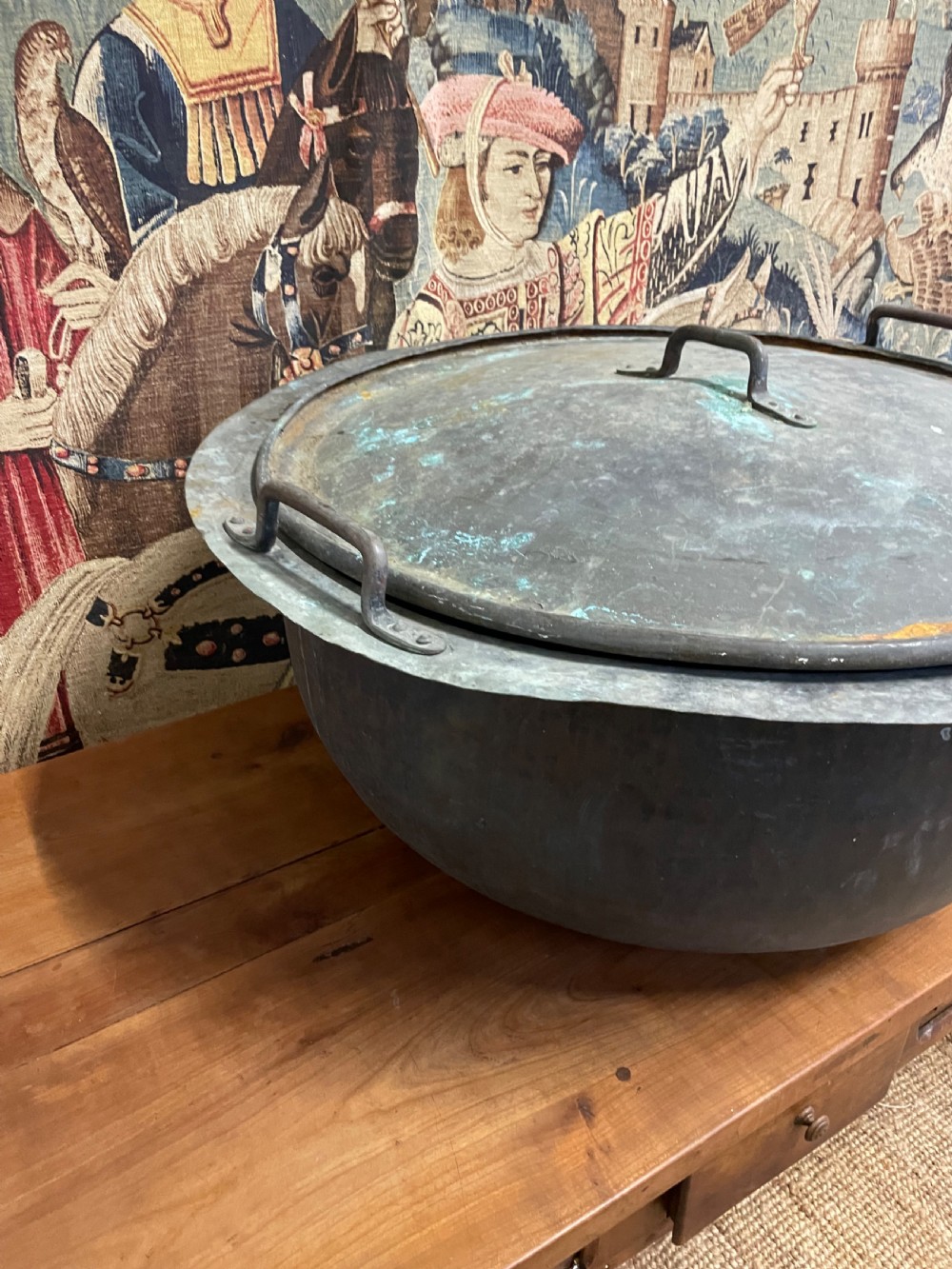A large round antique copper vessel featuring a fitted lid, twin iron loop handles, and a deep patinated surface with verdigris tones. View IV