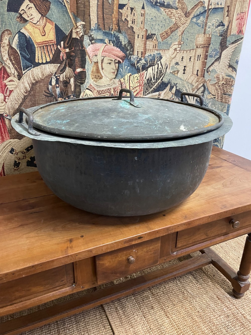 A large round antique copper vessel featuring a fitted lid, twin iron loop handles, and a deep patinated surface with verdigris tones. View VIII