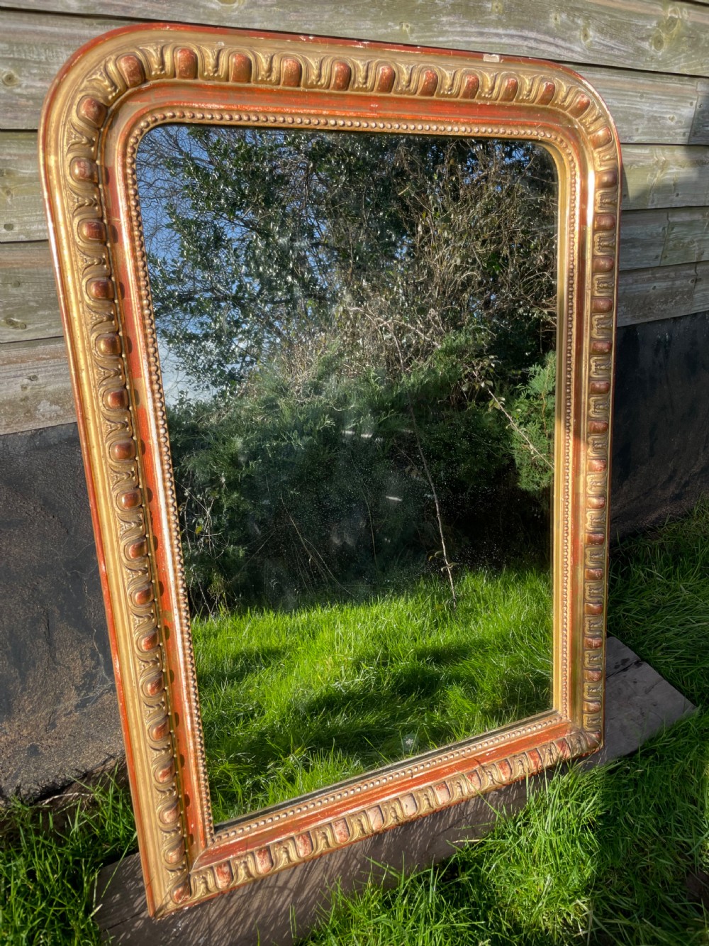 A 19th-century arched top wall mirror featuring a gadrooned and beaded gilt frame with visible red bole underlying the gold leaf.