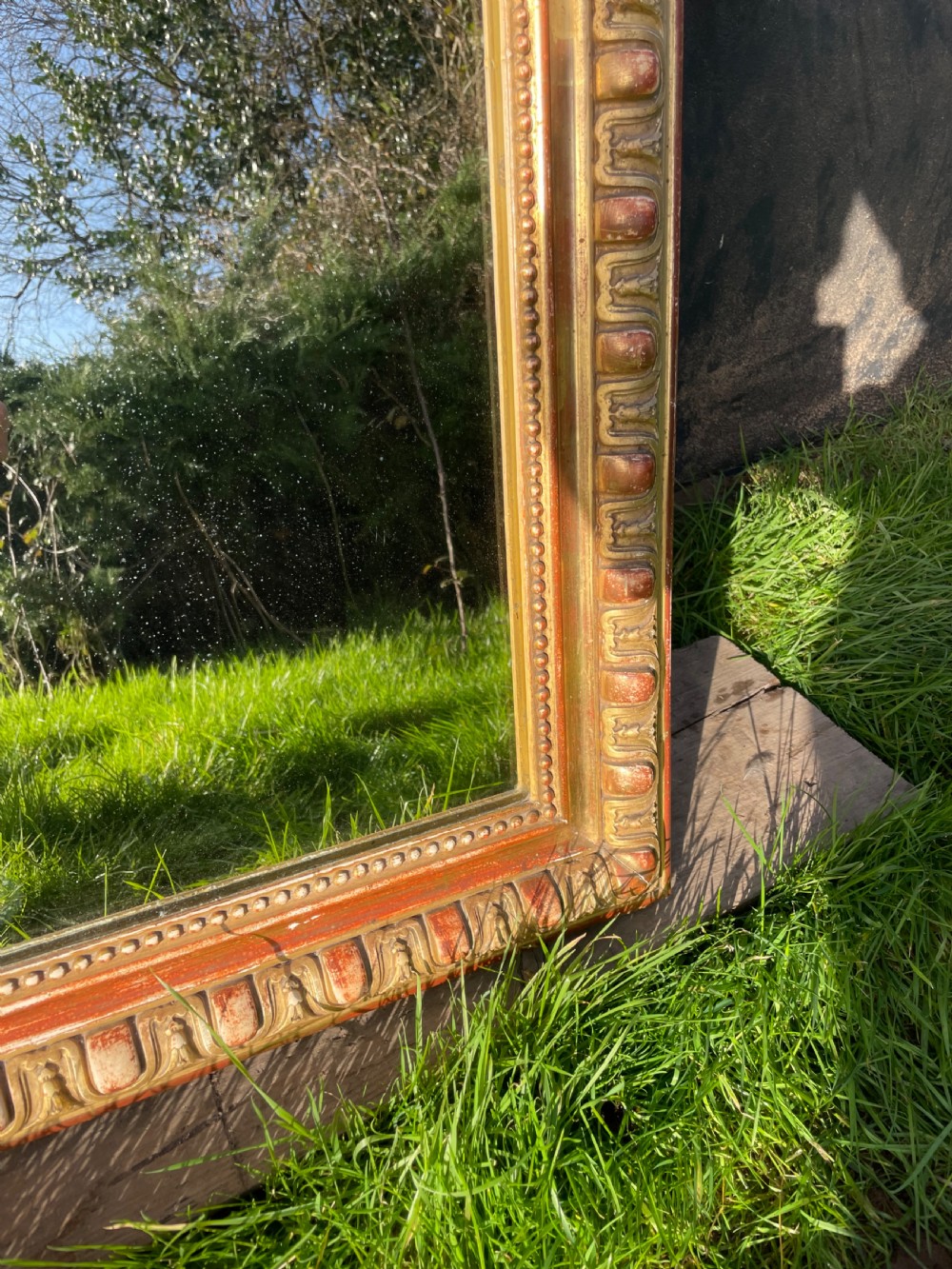 A 19th-century arched top wall mirror featuring a gadrooned and beaded gilt frame with visible red bole underlying the gold leaf. View V