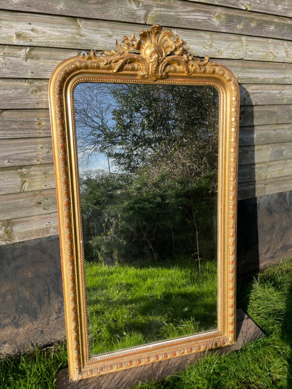 A large 19th-century gilded overmantle mirror featuring an arched top frame adorned with a carved floral shell crest and beaded inner moulding.
