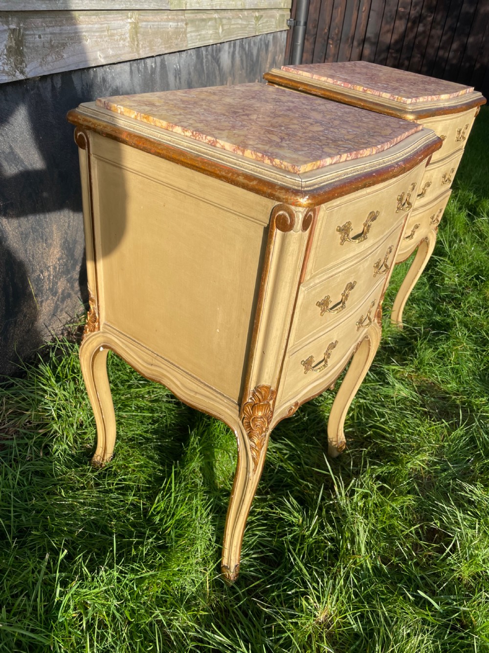 A pair of early 20th century French style cream painted and gilded bedside cabinets featuring fitted marble tops, three drawers, and carved cabriole legs. View II