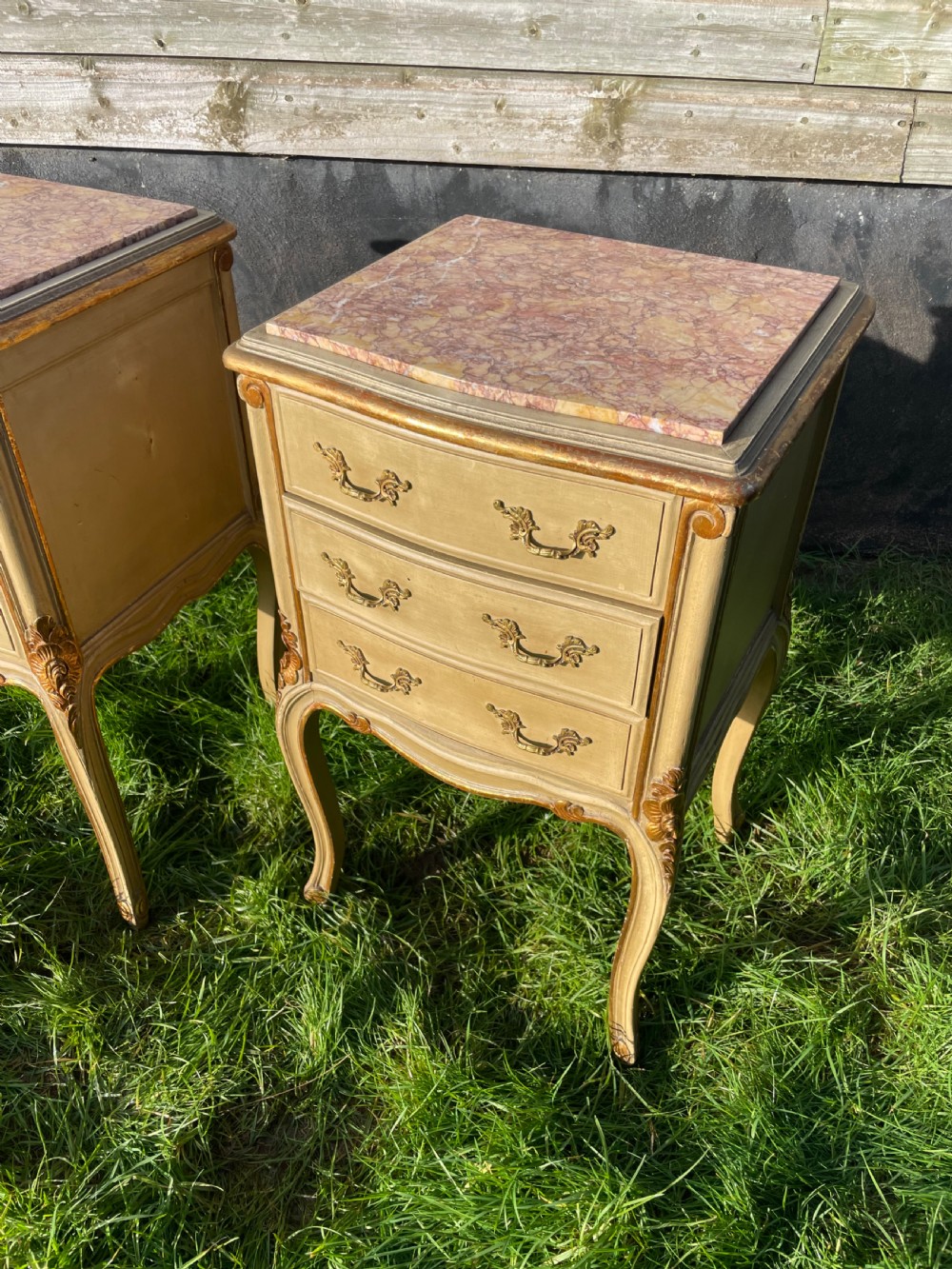 A pair of early 20th century French style cream painted and gilded bedside cabinets featuring fitted marble tops, three drawers, and carved cabriole legs. View III