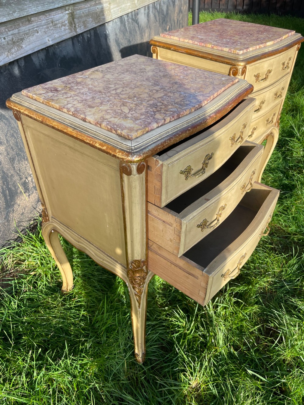 A pair of early 20th century French style cream painted and gilded bedside cabinets featuring fitted marble tops, three drawers, and carved cabriole legs. View VI