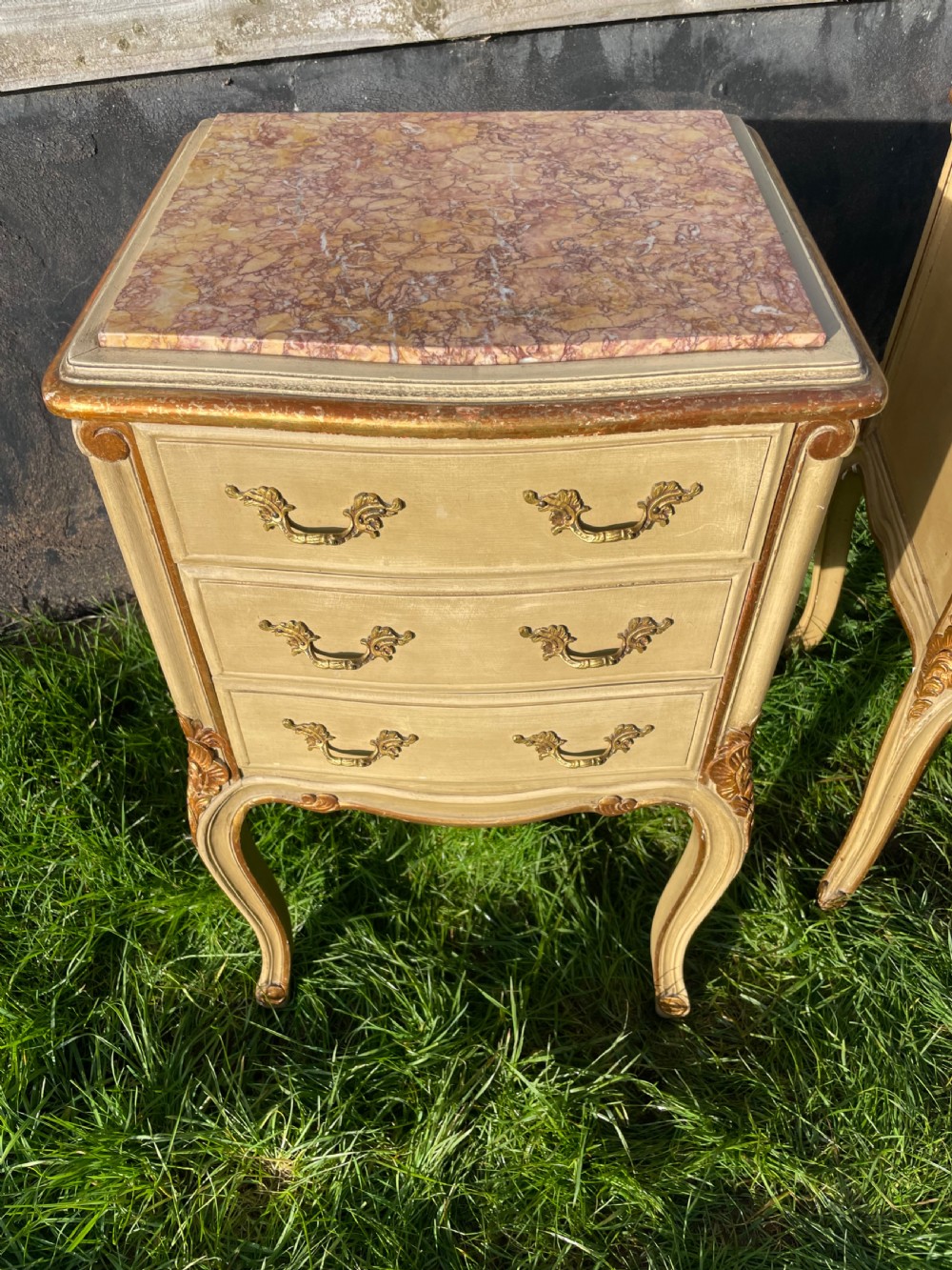 A pair of early 20th century French style cream painted and gilded bedside cabinets featuring fitted marble tops, three drawers, and carved cabriole legs. View VII