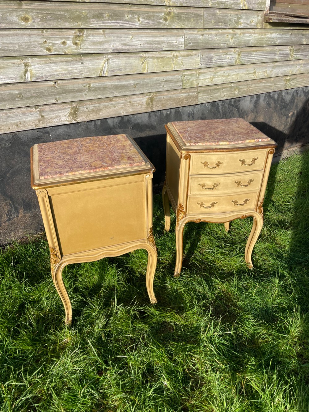 A pair of early 20th century French style cream painted and gilded bedside cabinets featuring fitted marble tops, three drawers, and carved cabriole legs. View IX