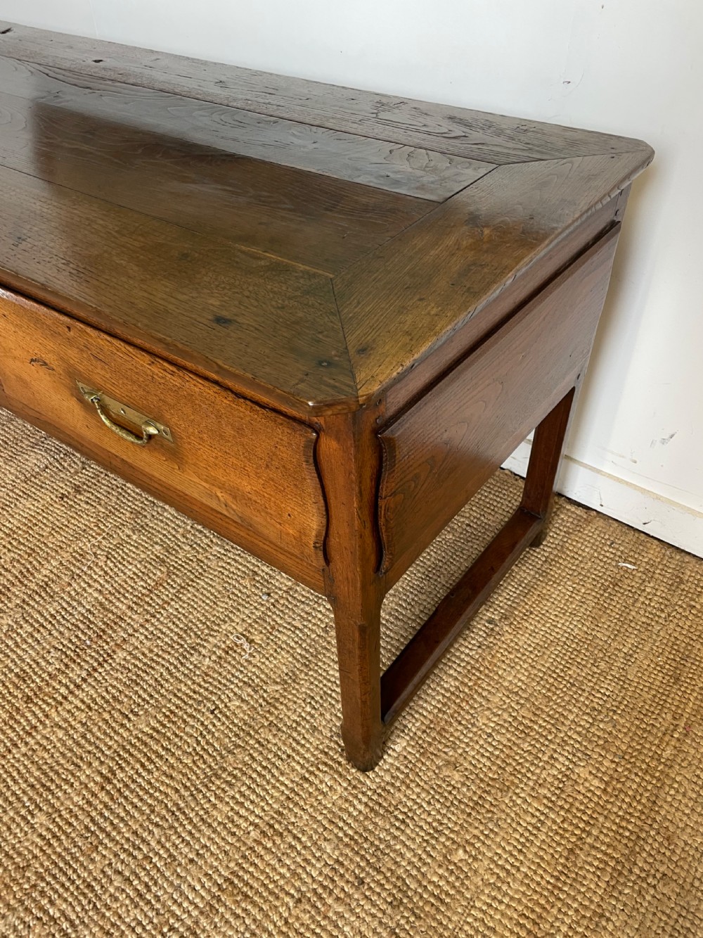An antique chestnut dresser base features a rectangular wooden top, three horizontal drawers with brass drop handles, and straight legs connected by stretchers. View IV