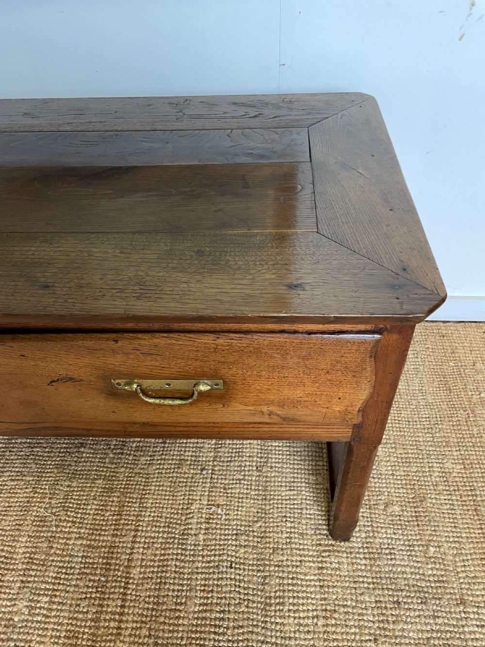 An antique chestnut dresser base features a rectangular wooden top, three horizontal drawers with brass drop handles, and straight legs connected by stretchers. View V