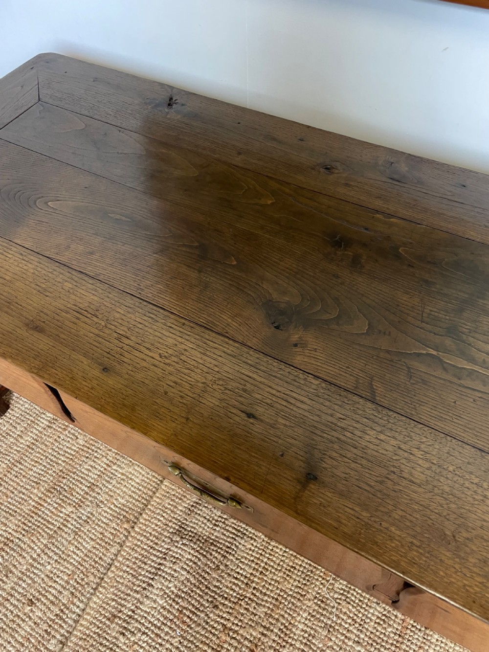 An antique chestnut dresser base features a rectangular wooden top, three horizontal drawers with brass drop handles, and straight legs connected by stretchers. View VIII