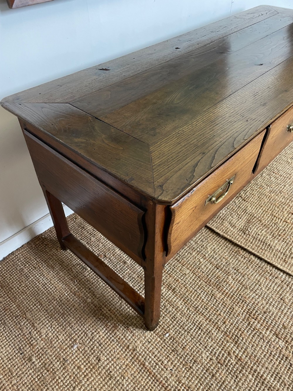 An antique chestnut dresser base features a rectangular wooden top, three horizontal drawers with brass drop handles, and straight legs connected by stretchers. View IX