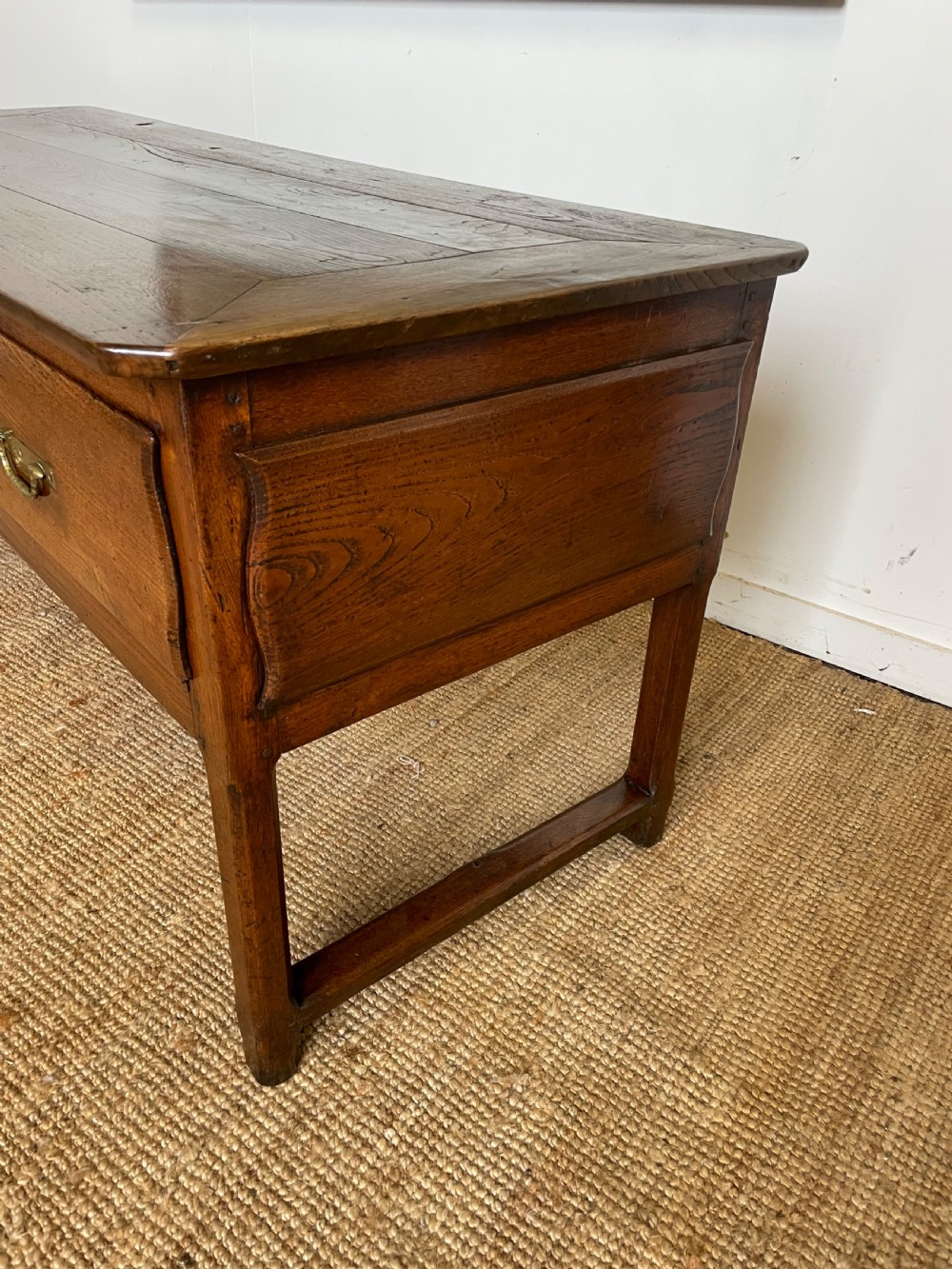 An antique chestnut dresser base features a rectangular wooden top, three horizontal drawers with brass drop handles, and straight legs connected by stretchers. View X