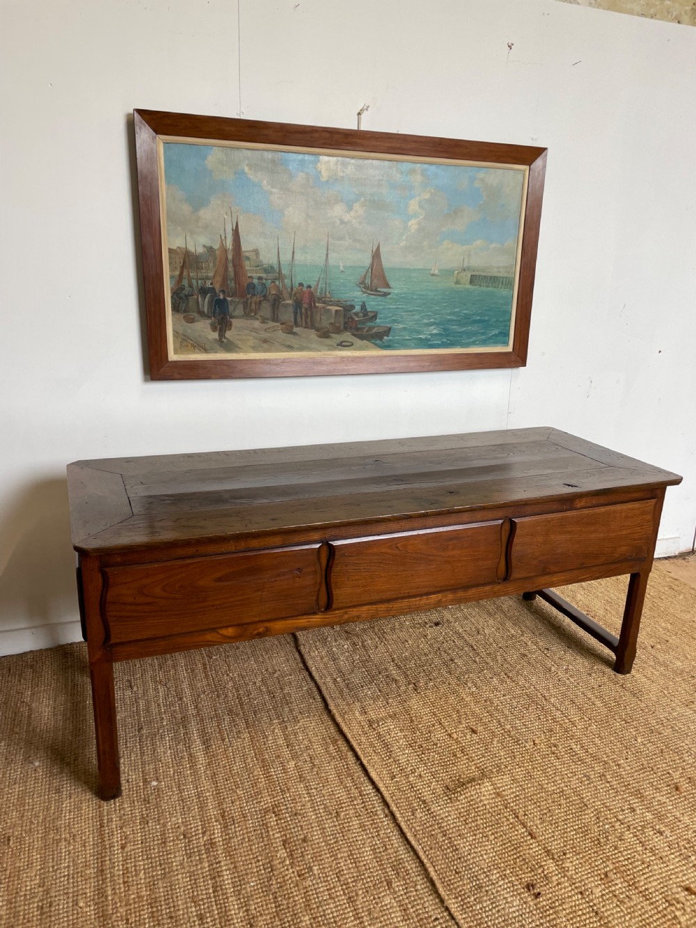 An antique chestnut dresser base features a rectangular wooden top, three horizontal drawers with brass drop handles, and straight legs connected by stretchers. View XI