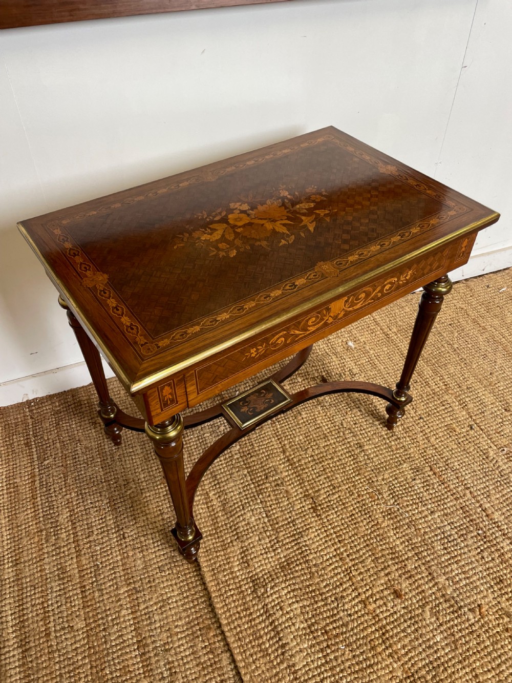 An overhead view of a French Napoleon III wooden side table featuring intricate floral marquetry on the top, slender turned legs, and brass edging.