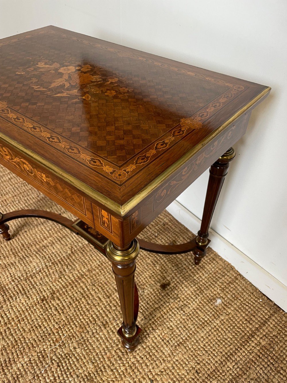 An overhead view of a French Napoleon III wooden side table featuring intricate floral marquetry on the top, slender turned legs, and brass edging. View II